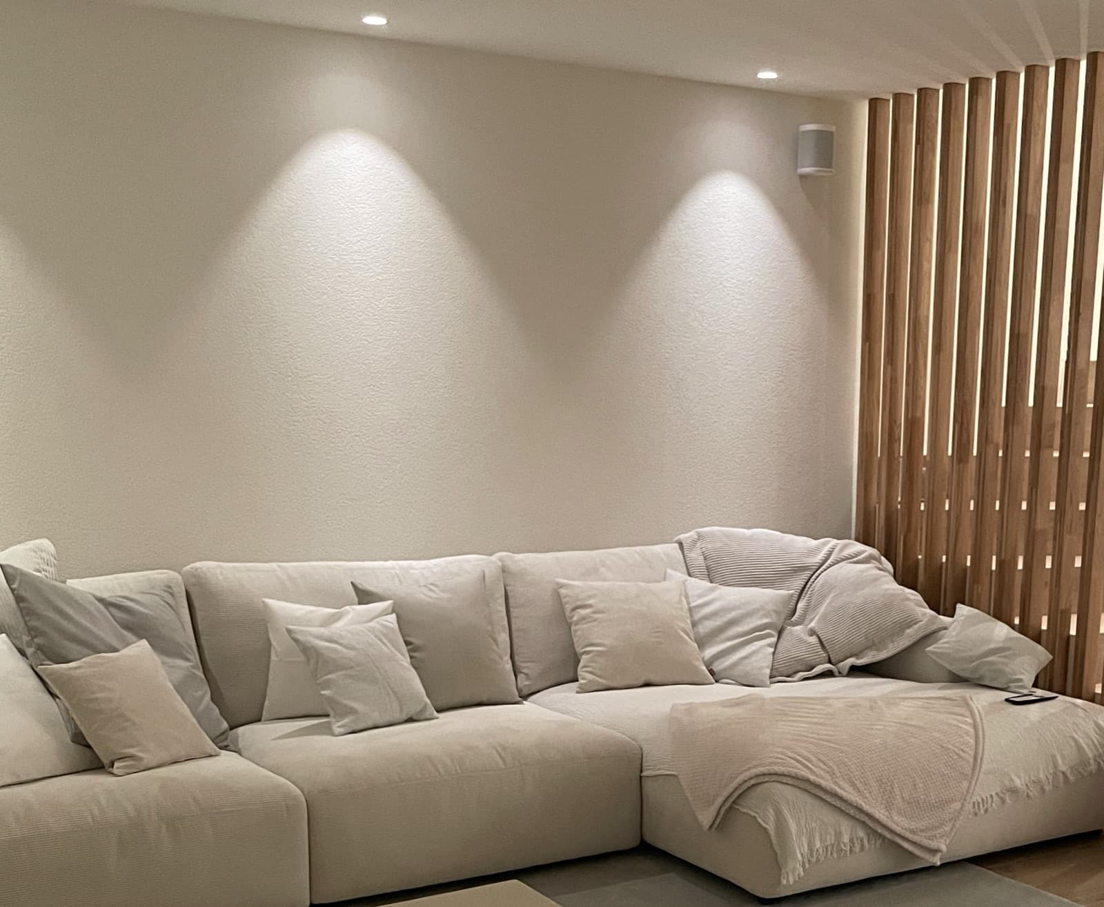 Wandfluter im Wohnzimmer zeichnen weiche Lichtkegel auf die Wand, dahinter eine hinterleuchtete Holzlamellenwand